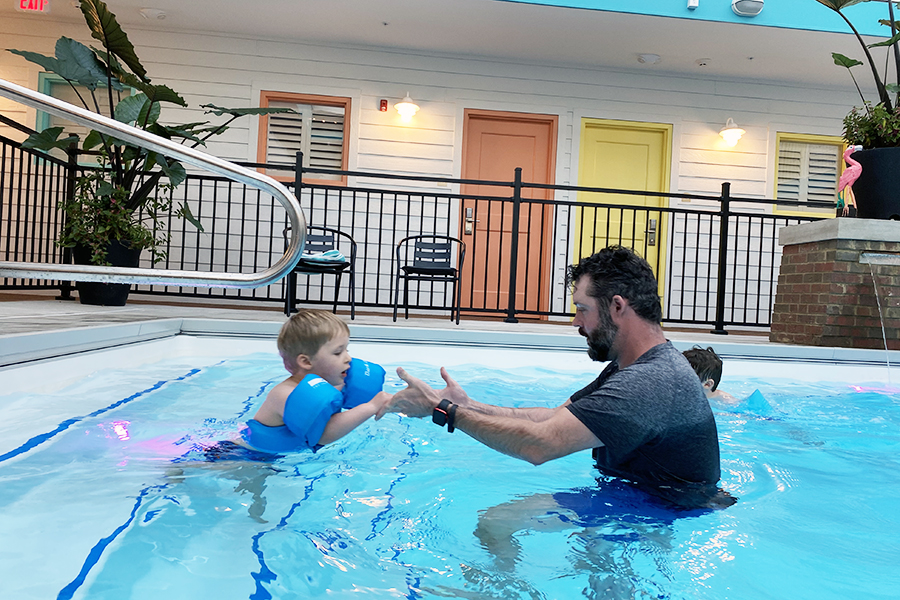 father helping son enter swimming pool